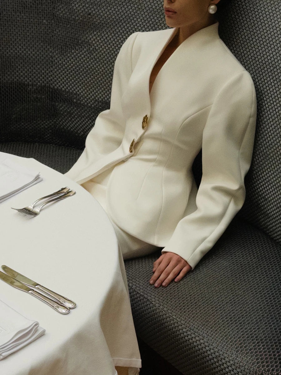Woman in a white outfit sitting at a table with cutlery in a restaurant setting