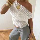 Person wearing a white polka dot top and gray pants with gold jewelry.