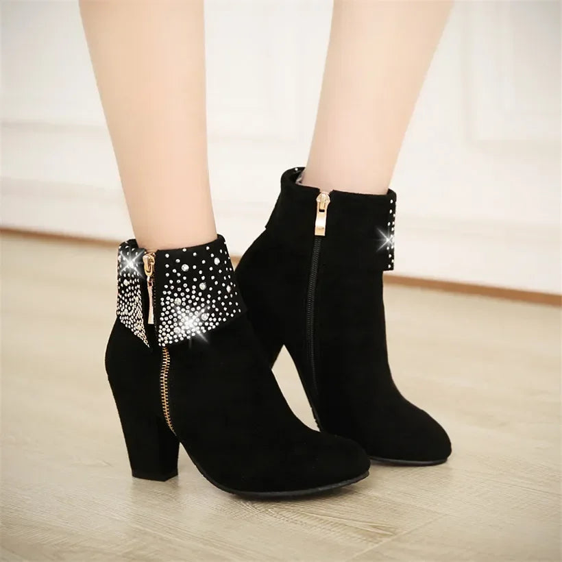 Black ankle boots with rhinestone accents on a light wooden floor.