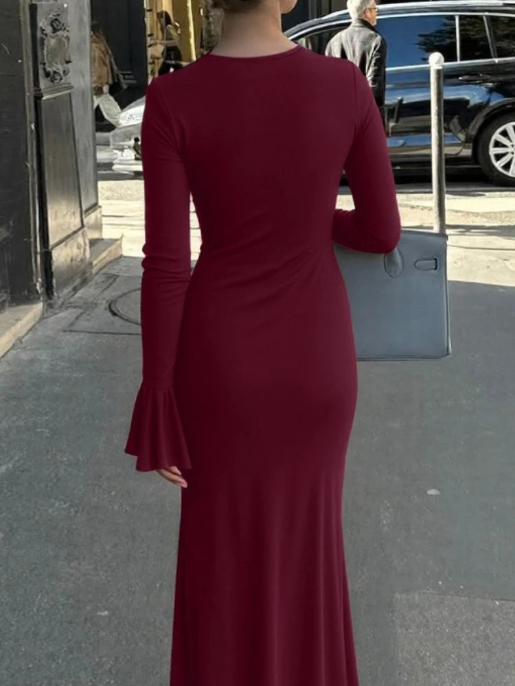 Person wearing a burgundy dress with long sleeves on a city street.