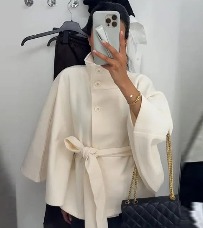 Person wearing a cream-colored coat with a black handbag in a mirror selfie.