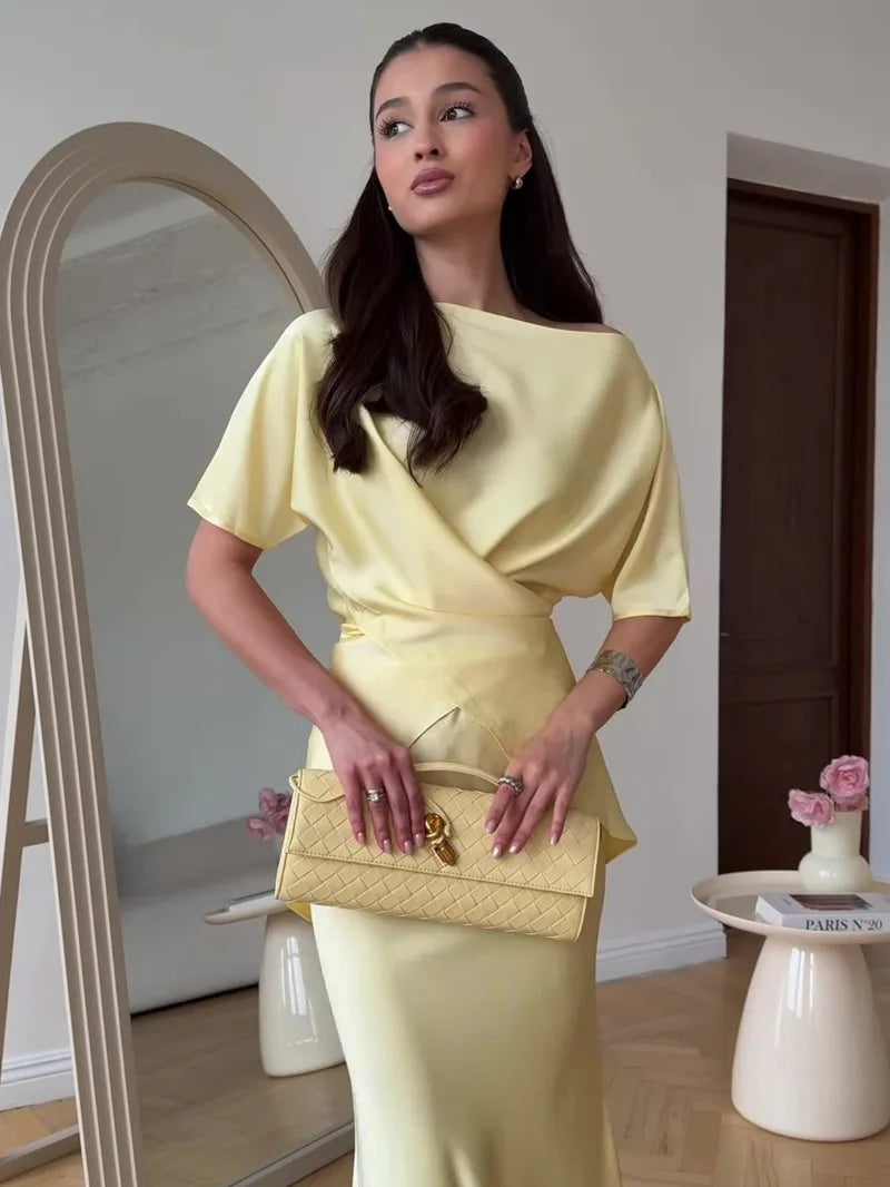 Woman in a yellow dress holding a matching handbag in a room with a mirror and small table.
