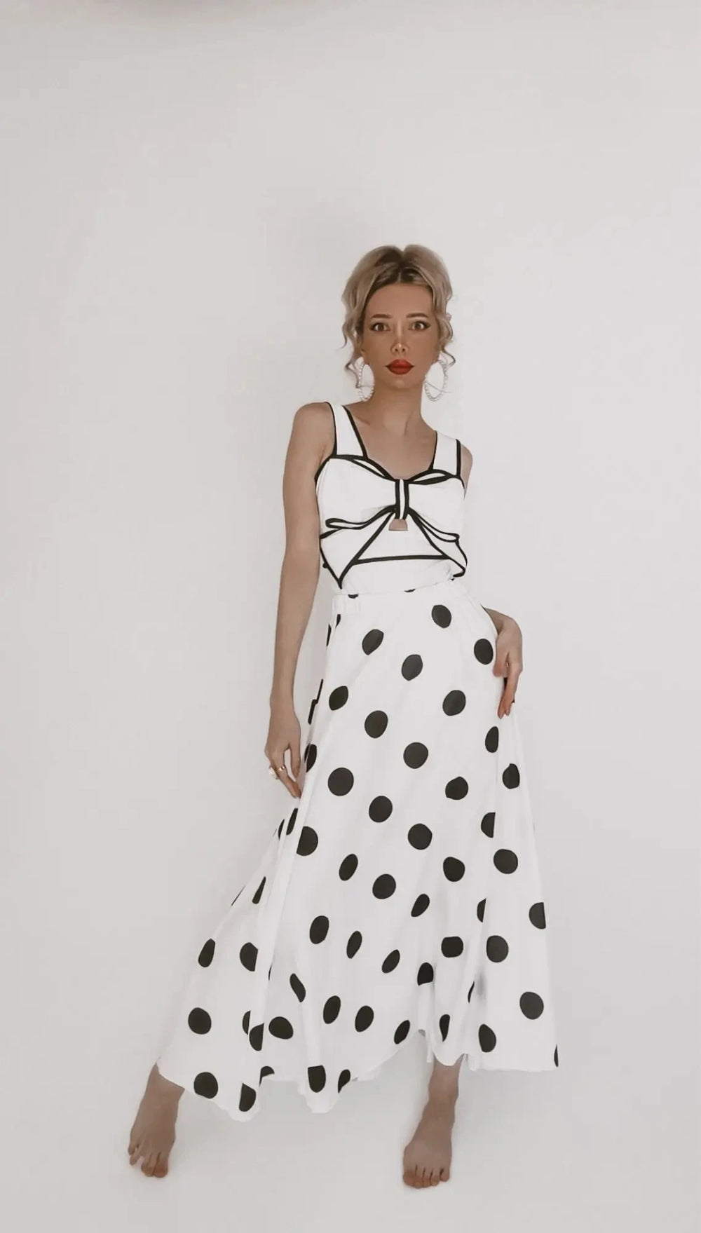 Woman in a white and black polka dot two-piece swimsuit featuring a bow detail on the top and a long flowing skirt.