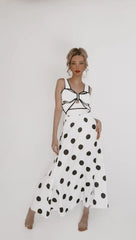 Woman in a white and black polka dot two-piece swimsuit featuring a bow detail on the top and a long flowing skirt.