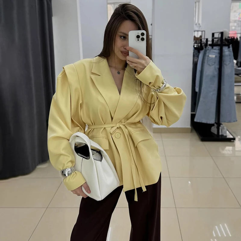 Woman taking a mirror selfie wearing a yellow coat in a store.