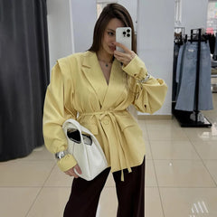 Woman taking a mirror selfie wearing a yellow coat in a store.
