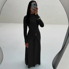 Person wearing a black dress with long sleeves and a slit, standing against a white background.
