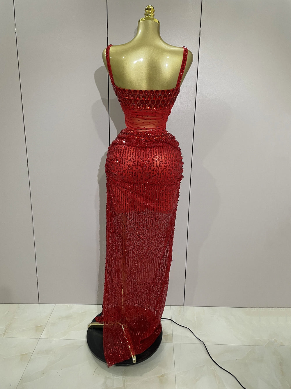 Red beaded evening gown on a mannequin against a white wall.