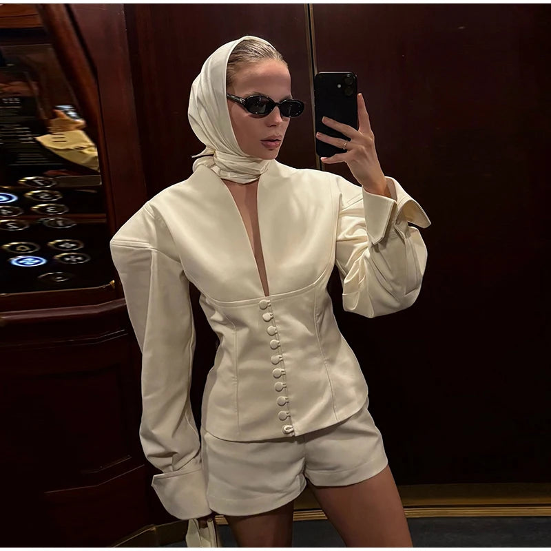 Person wearing a white outfit with a deep neckline and short shorts, taking a mirror selfie.