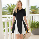 Woman wearing a black and white dress holding a beige handbag on a balcony with greenery.