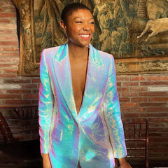 Person wearing a colorful iridescent blazer in front of a brick wall with tapestries.