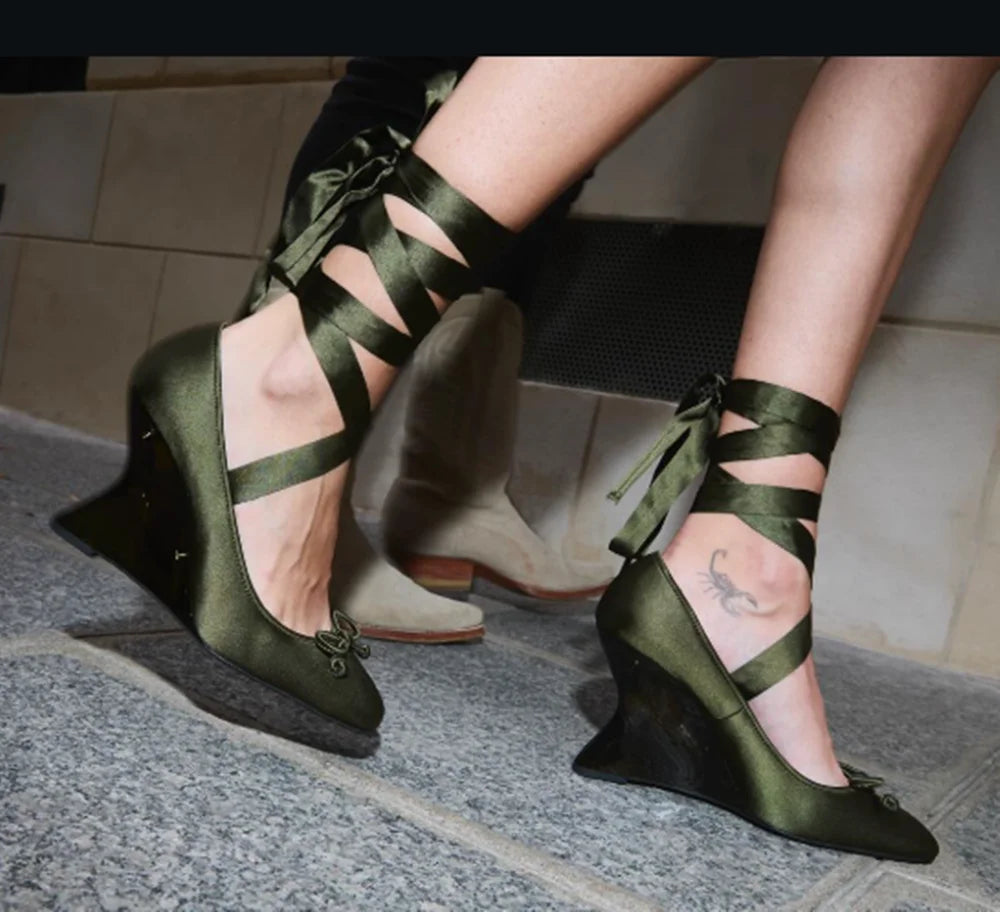 Green satin shoes with ribbon detailing worn by a person on a tiled floor.