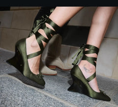 Green satin shoes with ribbon detailing worn by a person on a tiled floor.