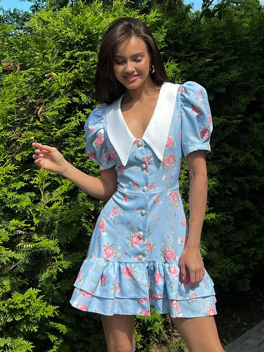 Light blue mini dress with a white pointed collar, short puff sleeves, pearl button front, and a tiered ruffled hem.