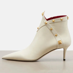 White leather pointed toe ankle boot with gold studs and thin heel, side view.