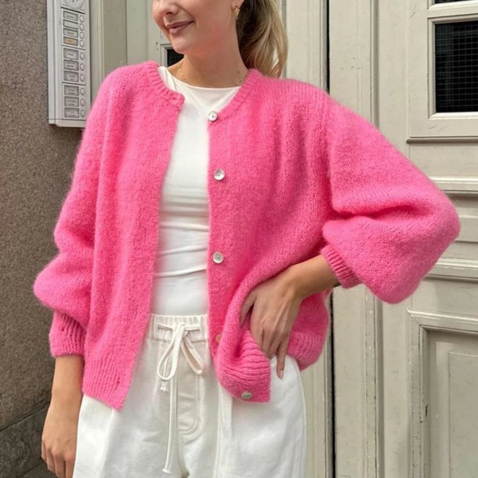 Person wearing a bright pink cardigan over a white outfit, standing against a neutral wall.