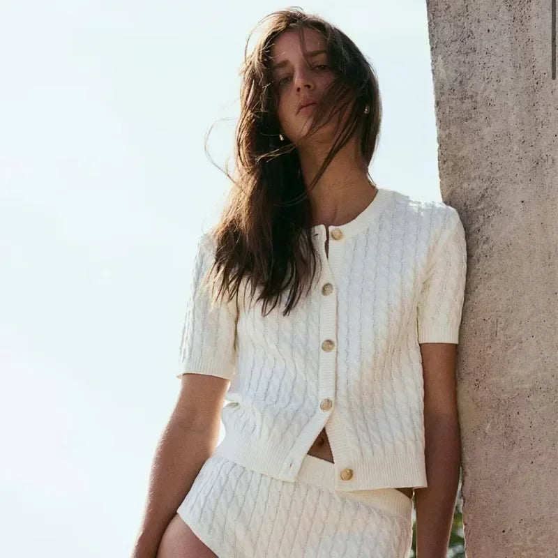 Woman wearing a white knit outfit leaning against a stone wall.