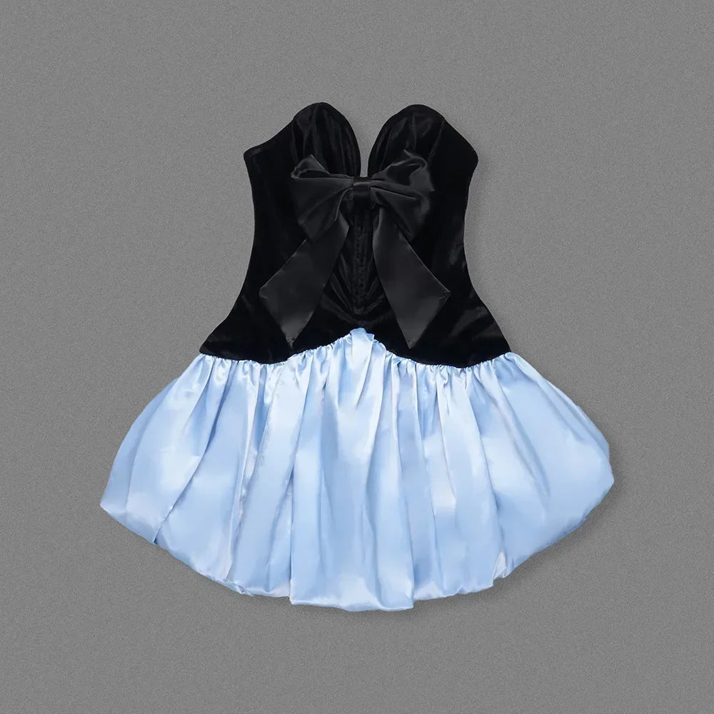 Black velvet top with a large bow and light blue skirt on a gray background