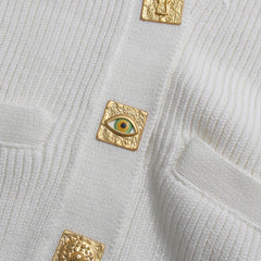 Gold square brooches with eye design on a textured light gray fabric background