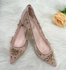 Pink high-heeled shoes with embellishments on a white textured surface with a peach rose.