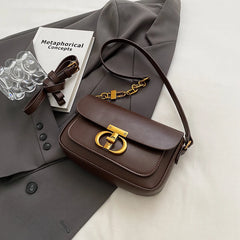 Brown handbag with gold clasp on a gray suit jacket with a book and glasses.