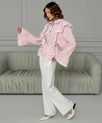 Woman wearing a pink ruffled blouse and white pants in a room with a gray sofa.