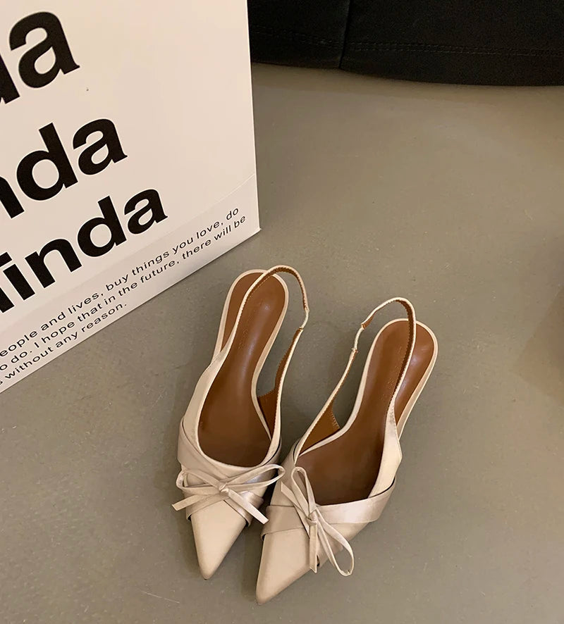 Pair of beige high heels with ribbon details on a neutral background