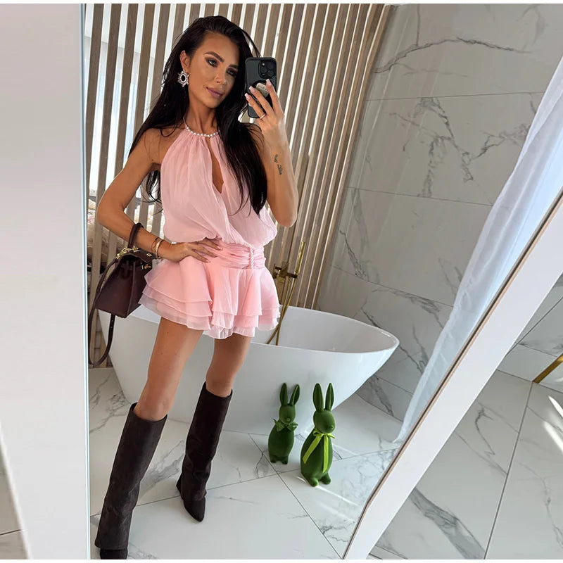 Woman taking a mirror selfie wearing a pink dress and black boots in a modern bathroom.