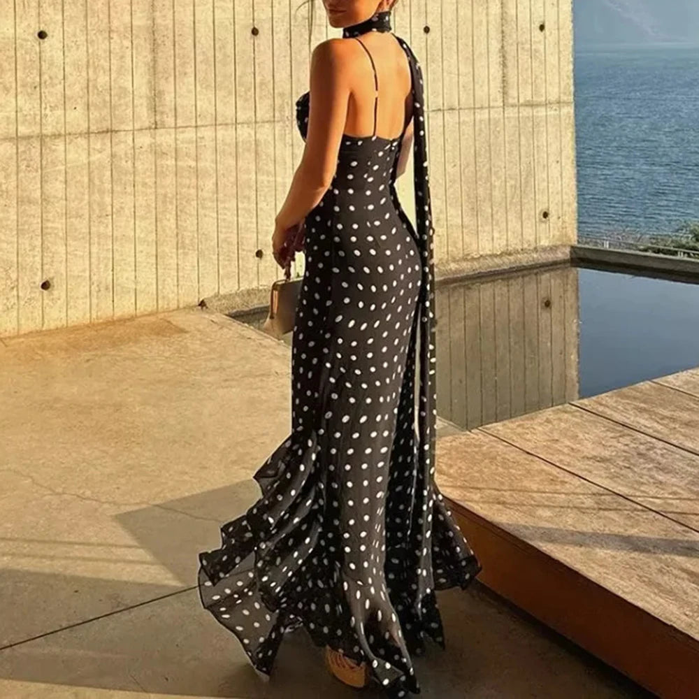 Woman in a black polka dot dress standing by a pool with ocean view