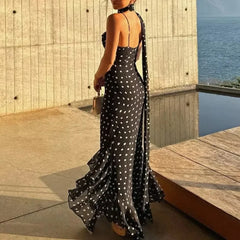 Woman in a black polka dot dress standing by a pool with ocean view