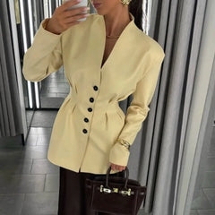Person wearing a light yellow blazer with black buttons, holding a brown handbag indoors.