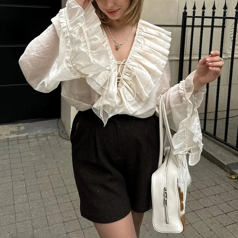 Person wearing a white ruffled blouse and black shorts, holding a white handbag.
