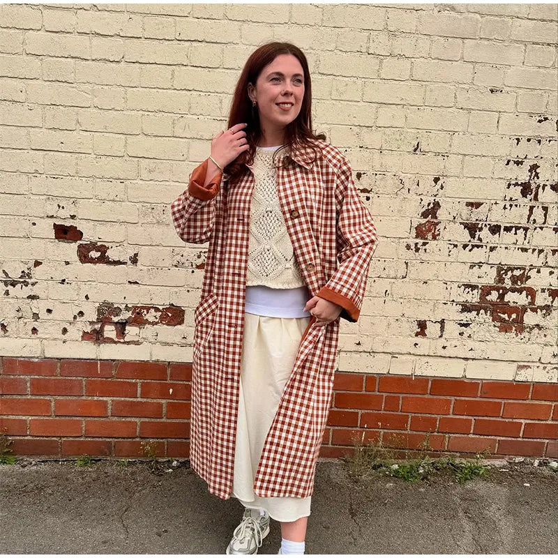 Woman wearing a red and white checkered coat against a textured wall.