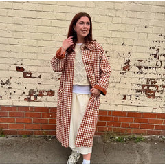Woman wearing a red and white checkered coat against a textured wall.