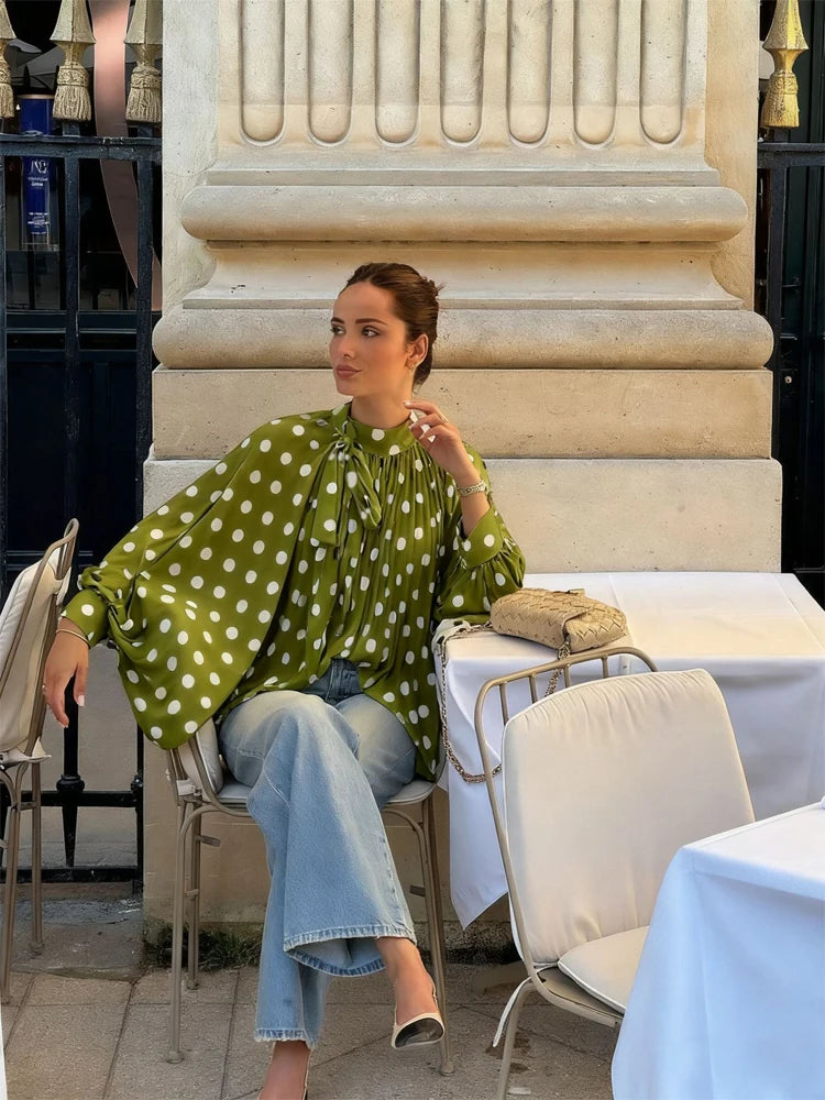 Woman in a green polka dot blouse and jeans sitting at an outdoor cafe table.