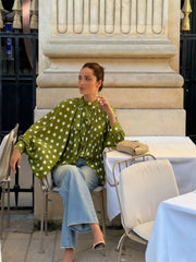 Woman in a green polka dot blouse and jeans sitting at an outdoor cafe table.