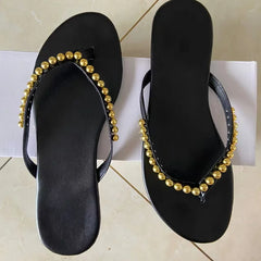Pair of black flat embellished flip flops on a white surface.