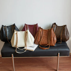 Five handbags of different colors arranged on a black bench.