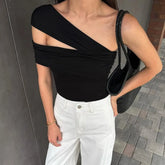 Person wearing a black off-shoulder top and white pants, holding a black bag.