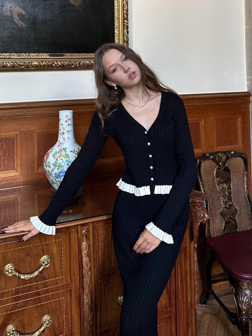 Woman in a black outfit standing in an elegant room with wooden furniture and decorative elements.