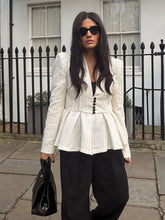 Woman wearing a white peplum top and black pants standing in front of a black iron fence.