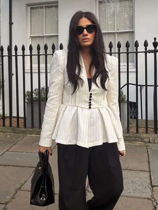 Woman wearing a white peplum top and black pants standing in front of a black iron fence.