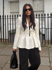 Woman wearing a white peplum top and black pants standing in front of a black iron fence.