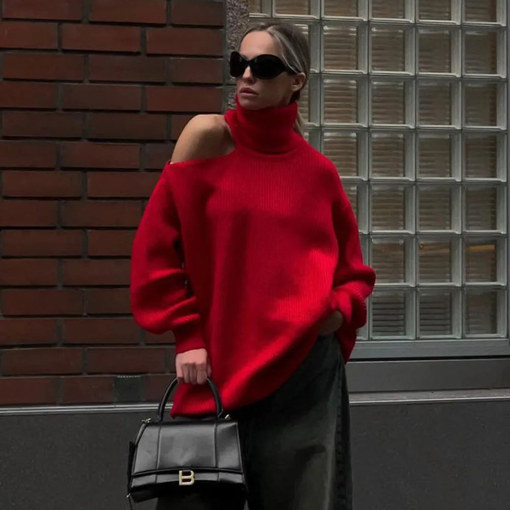 Woman wearing a red sweater and sunglasses, holding a black handbag against a brick wall.