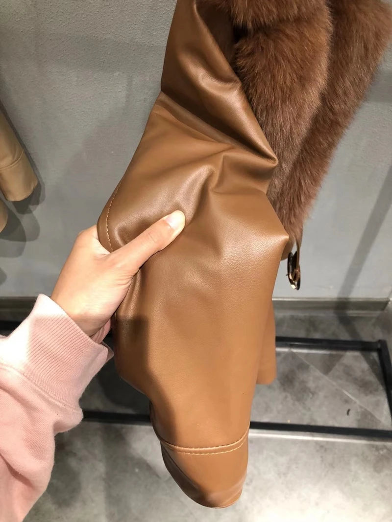 Brown leather glove held by a hand against a neutral background