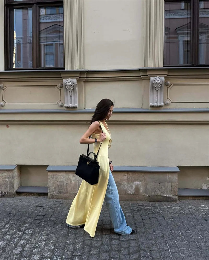 Woman in a yellow dress and blue jeans walking on a street with a building in the background