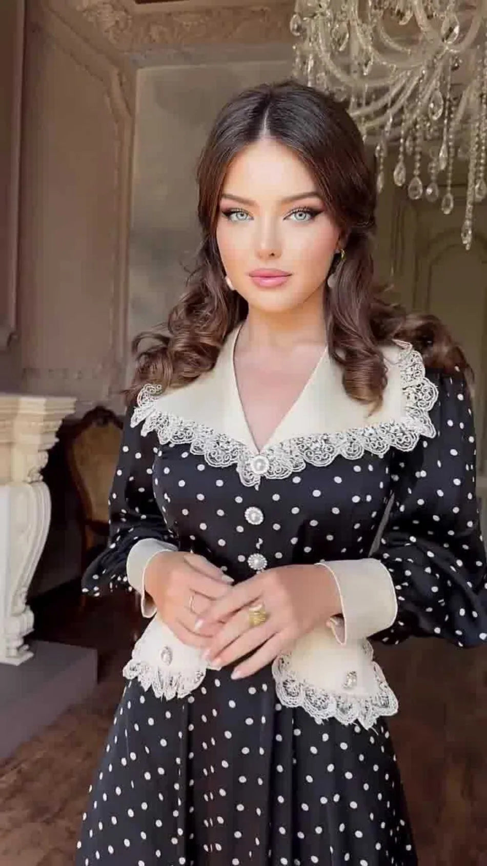 Woman wearing a black polka dot dress with white lace details in an elegant interior setting.