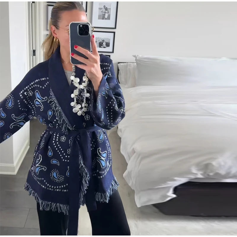 Woman wearing a blue patterned robe taking a mirror selfie in a bedroom.