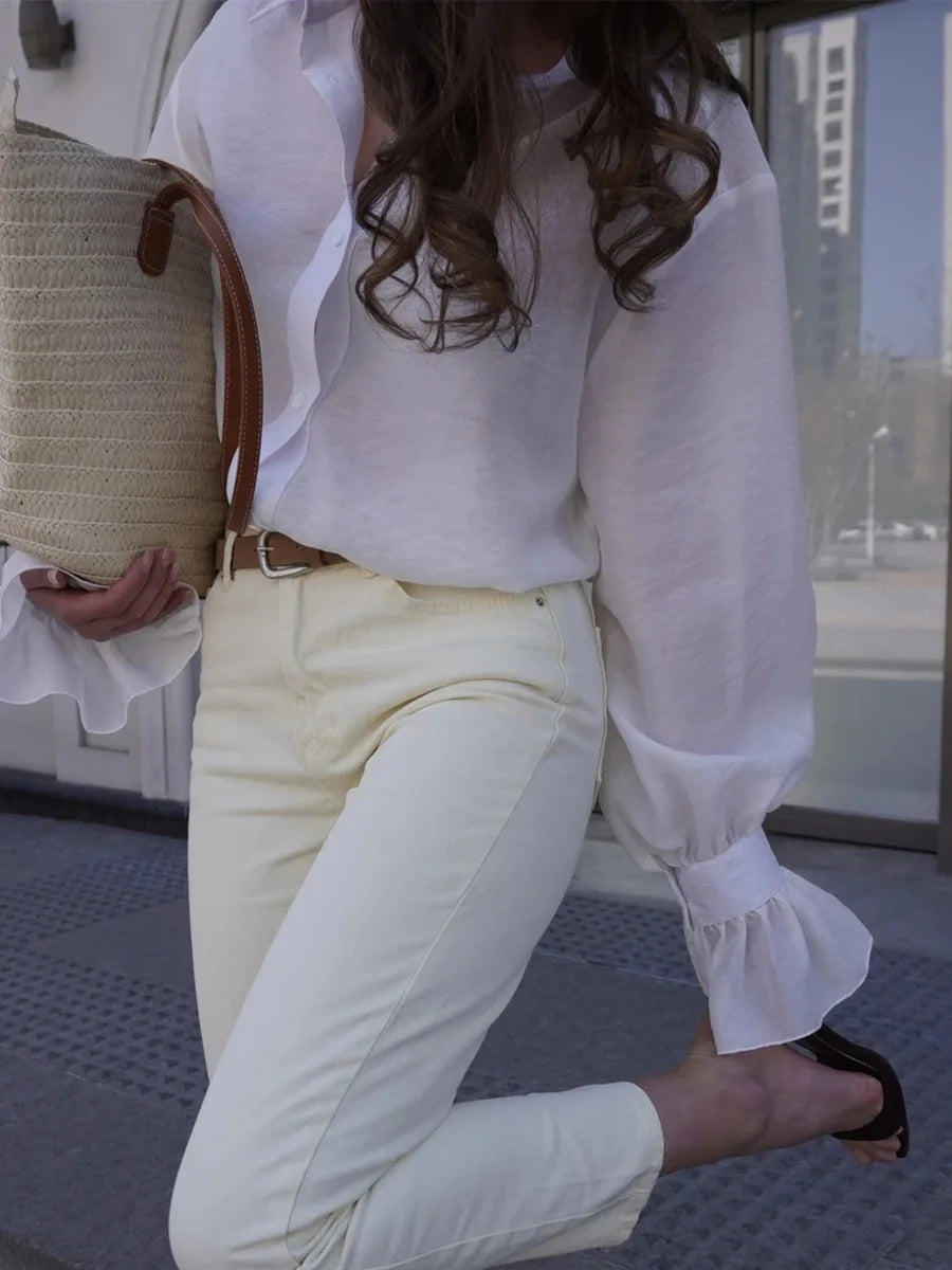 Person wearing a white blouse and light-colored pants with a straw bag.