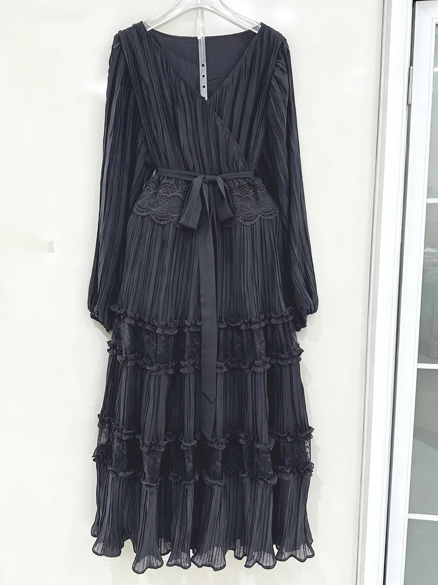 Black pleated dress with lace details on a hanger against a white wall.